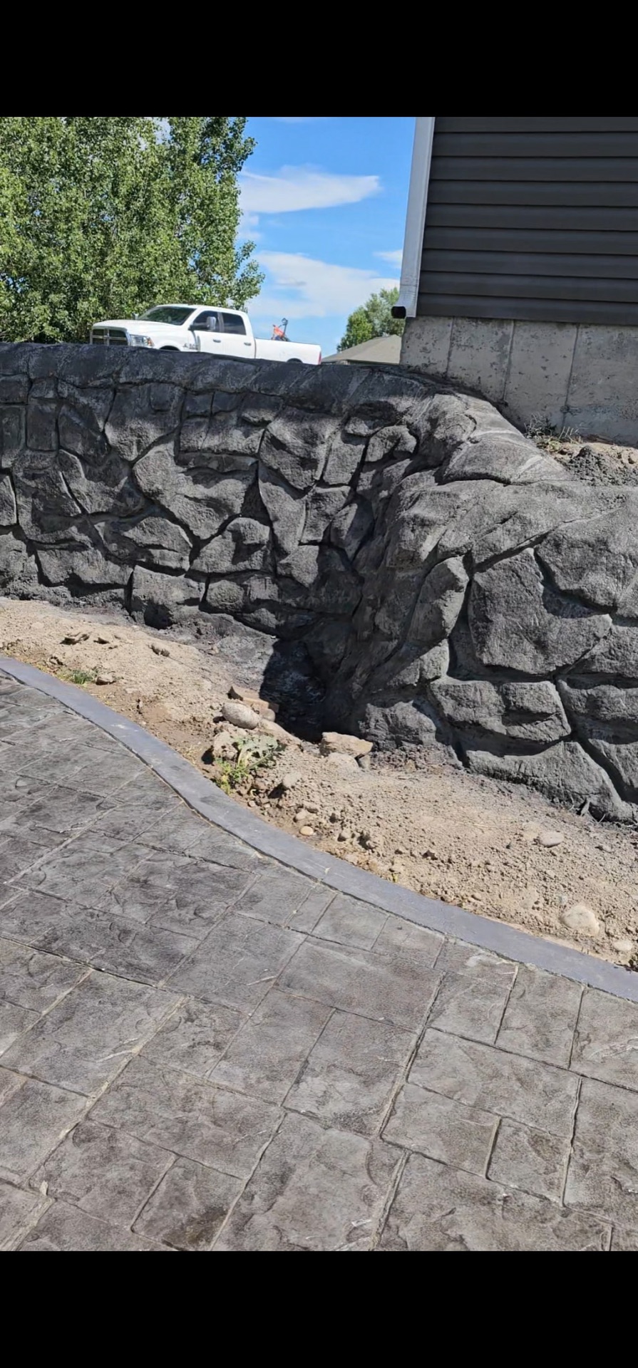 Dark grey stamped concrete walkway beside a stamped rock-face concrete retaining wall in Eastern Idaho by Skinner Customs